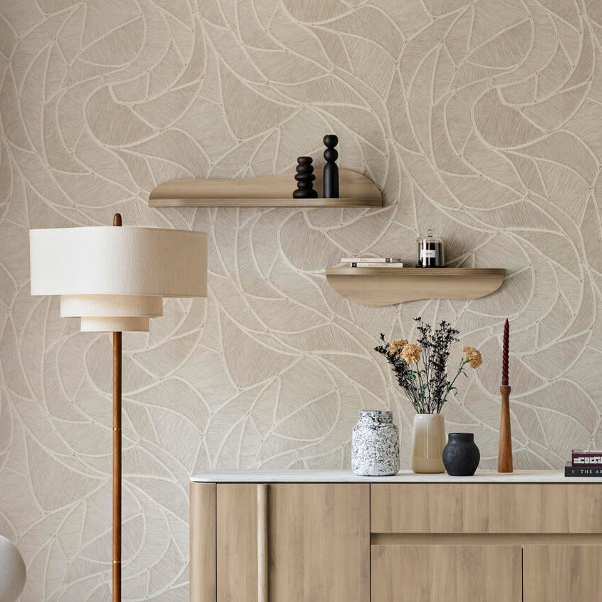 A styled interior scene showing a light wood sideboard or credenza against a beige patterned wallpaper wall, with a floor lamp, chair, rug, and staircase visible in a real room setting.