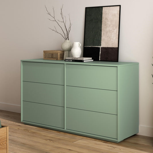 A sage green 6-drawer dresser in a modern bedroom setting, styled with vases, a basket, and a framed print.